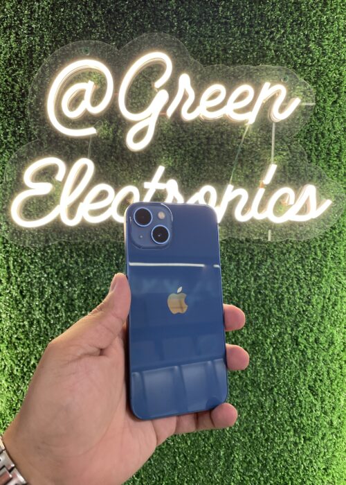 iPhone 13 color Azul Medianoche mostrando su sistema de doble cámara diagonal y el notch reducido, sobre una superficie reflectante con luz cálida. Disponible en Green Electronics