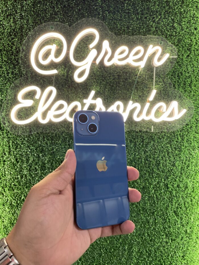 iPhone 13 color Azul Medianoche mostrando su sistema de doble cámara diagonal y el notch reducido, sobre una superficie reflectante con luz cálida. Disponible en Green Electronics