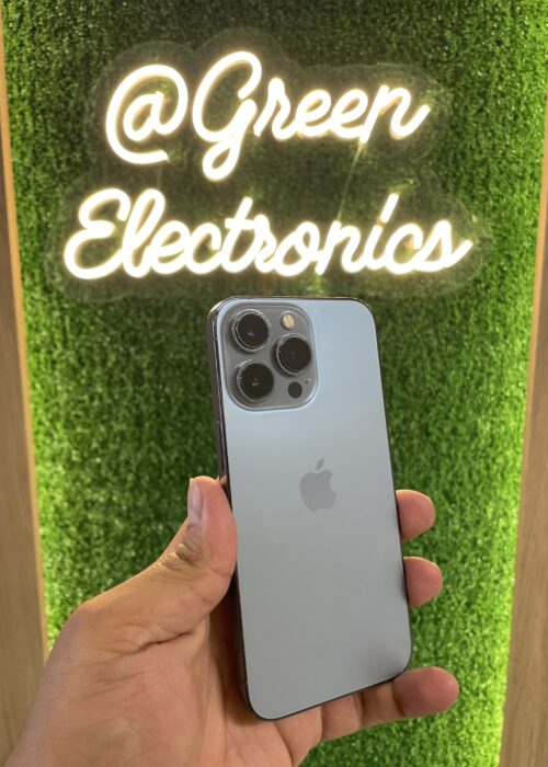 iPhone 13 Pro azul sierra en mano frente a letrero Green Electronics
