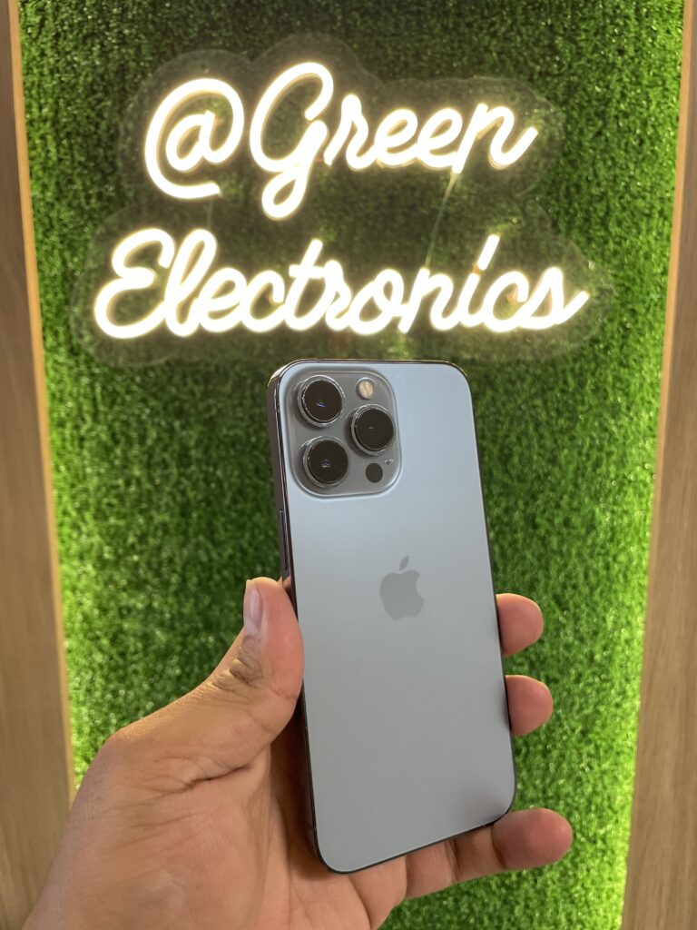 iPhone 13 Pro azul sierra en mano frente a letrero Green Electronics