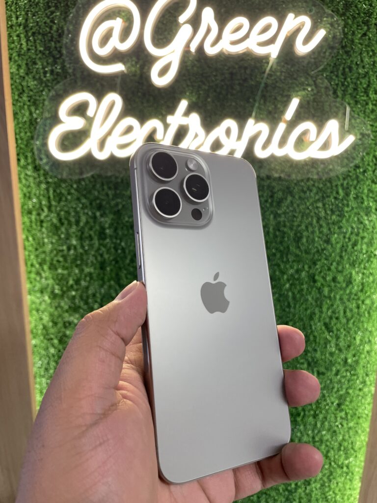 Celular usado en Colombia de alta calidad iPhone 15 Pro Max azul en mano frente a letrero Green Electronics