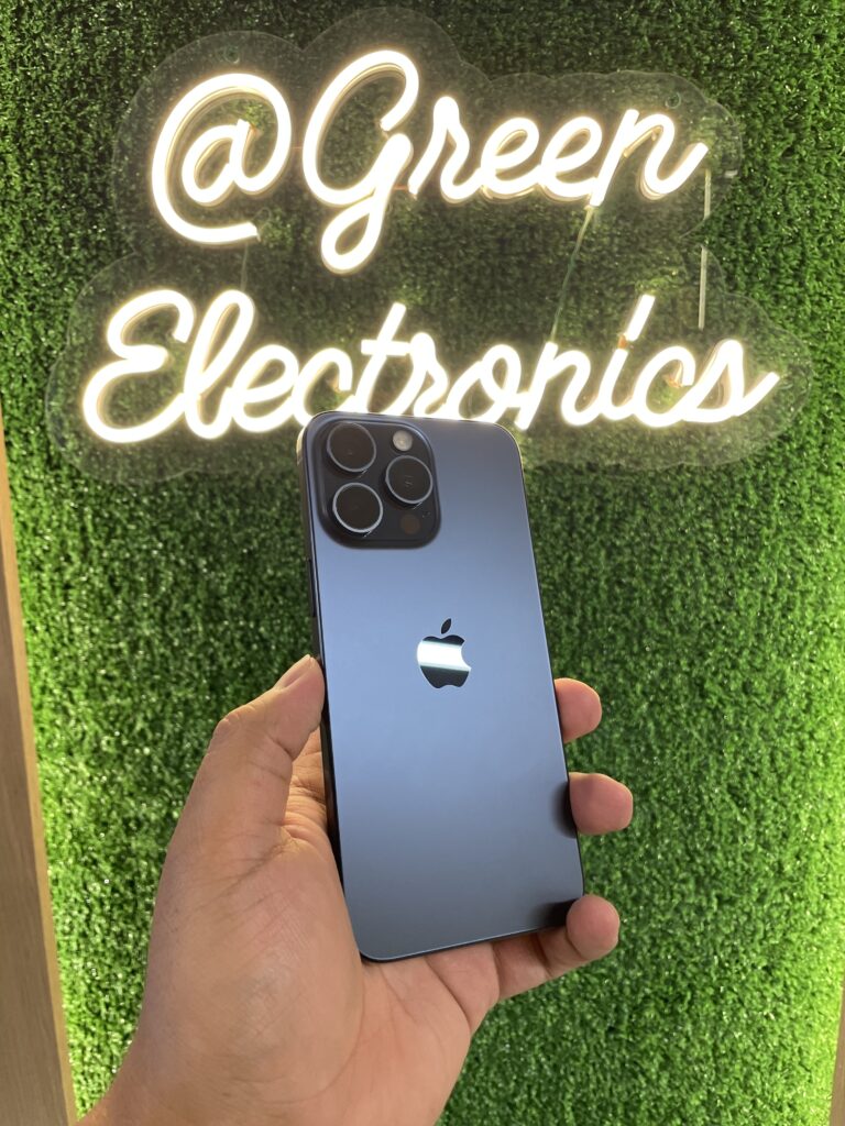 Celular usado en Colombia de alta calidad iPhone 15 Pro Max azul en mano frente a letrero Green Electronics
